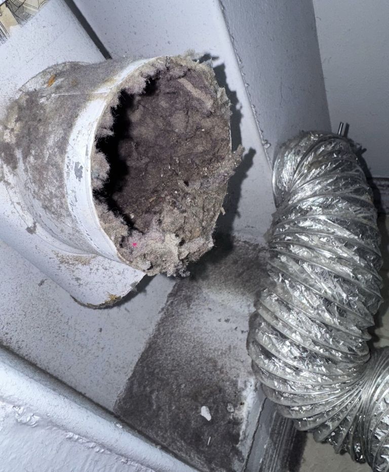 Dryer vent opening packed with lint, next to a foil dryer hose